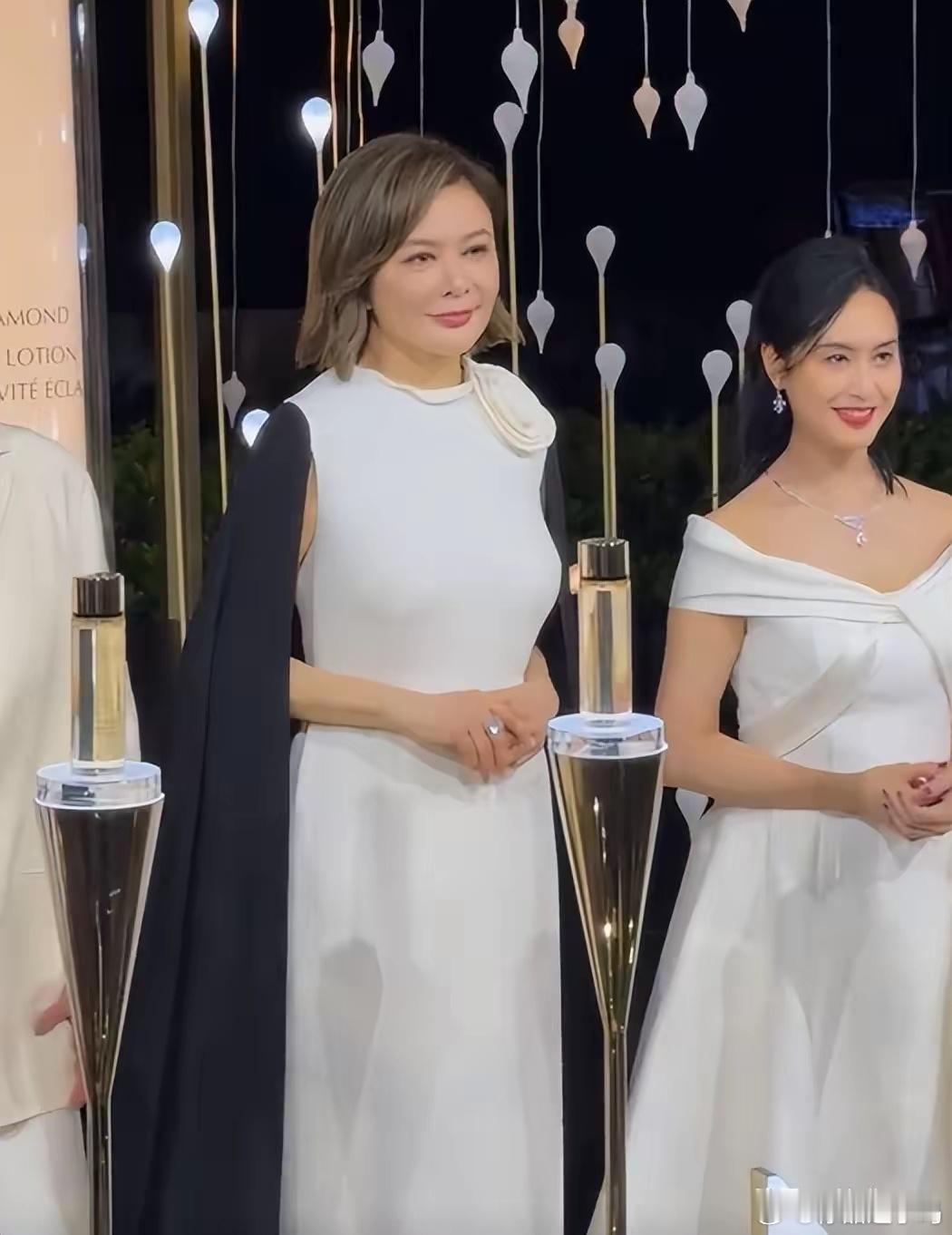 香港著名女星关之琳、朱茵受邀出席某品牌的活动。关之琳穿着白色无袖连衣裙搭配黑色披