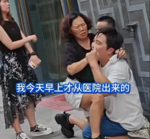 南京街头，一名男子跪在水泥地上，情绪激动地对着妻子连磕三个响头，哽咽着喊道：“我