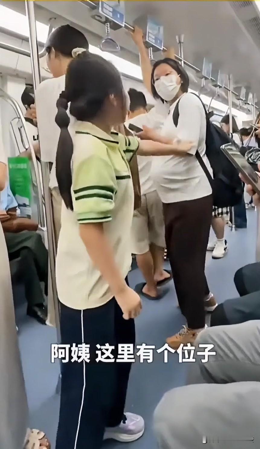地铁车厢内，一位孕妇背着包，一只手抓着顶部横扶手，另一只手拿着手机在看。旁边的小