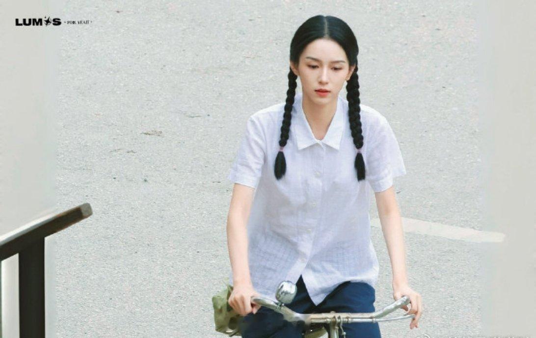 周也今日份新剧《红舞鞋》最新路透来了，扎着双马尾辫子、穿着白衬衫、骑着二八大杠