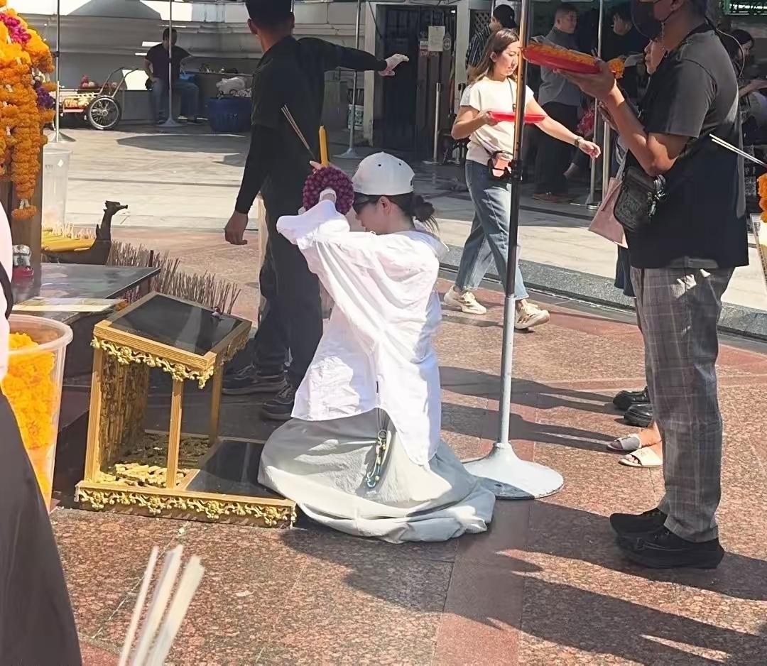 戚薇李承铉现身曼谷，戚薇身穿白色衬衣，头戴白色棒球帽，在佛前许愿，跪地虔诚祈祷，