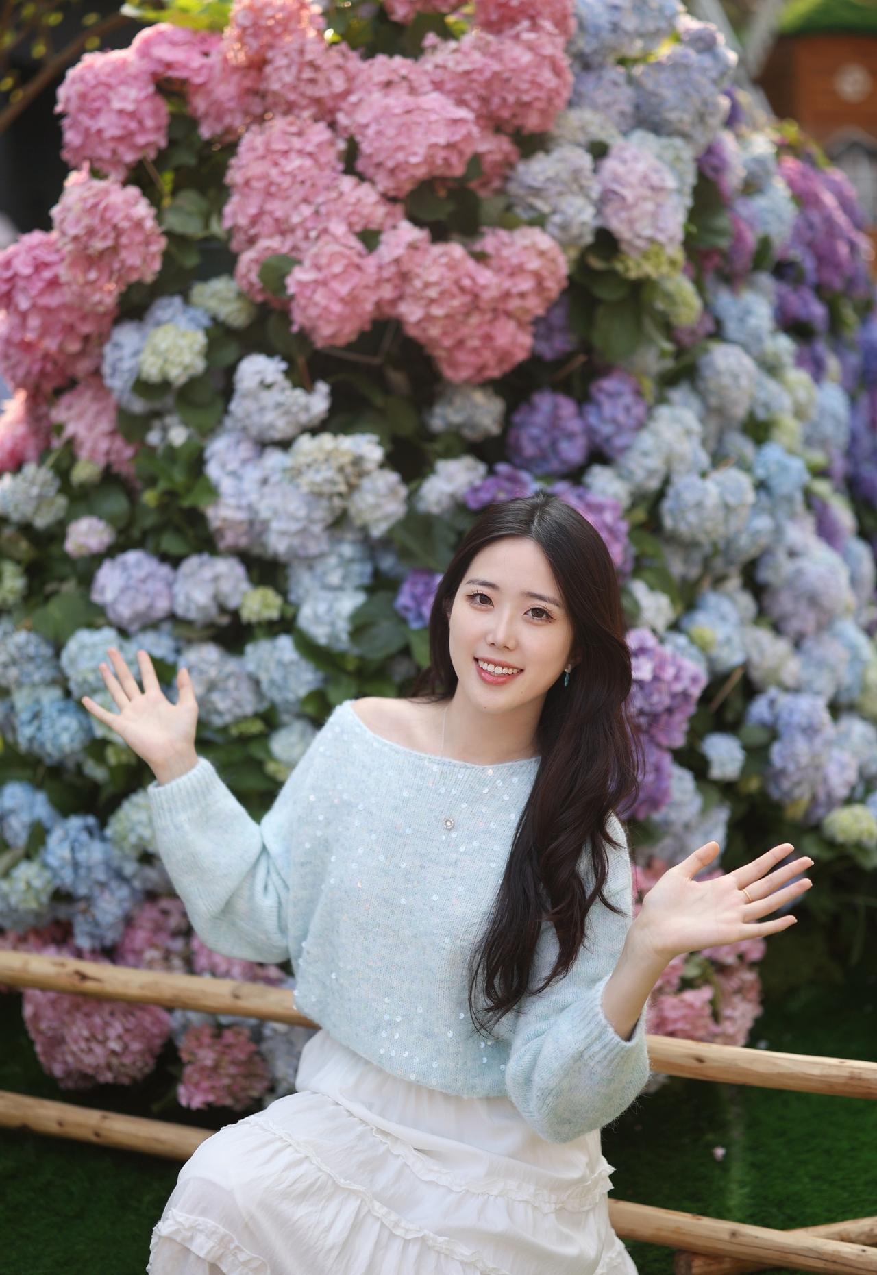 浅蓝色带亮片的露肩毛衣＋白色长裙，长发披肩，面带微笑，感受着绣球花的美。