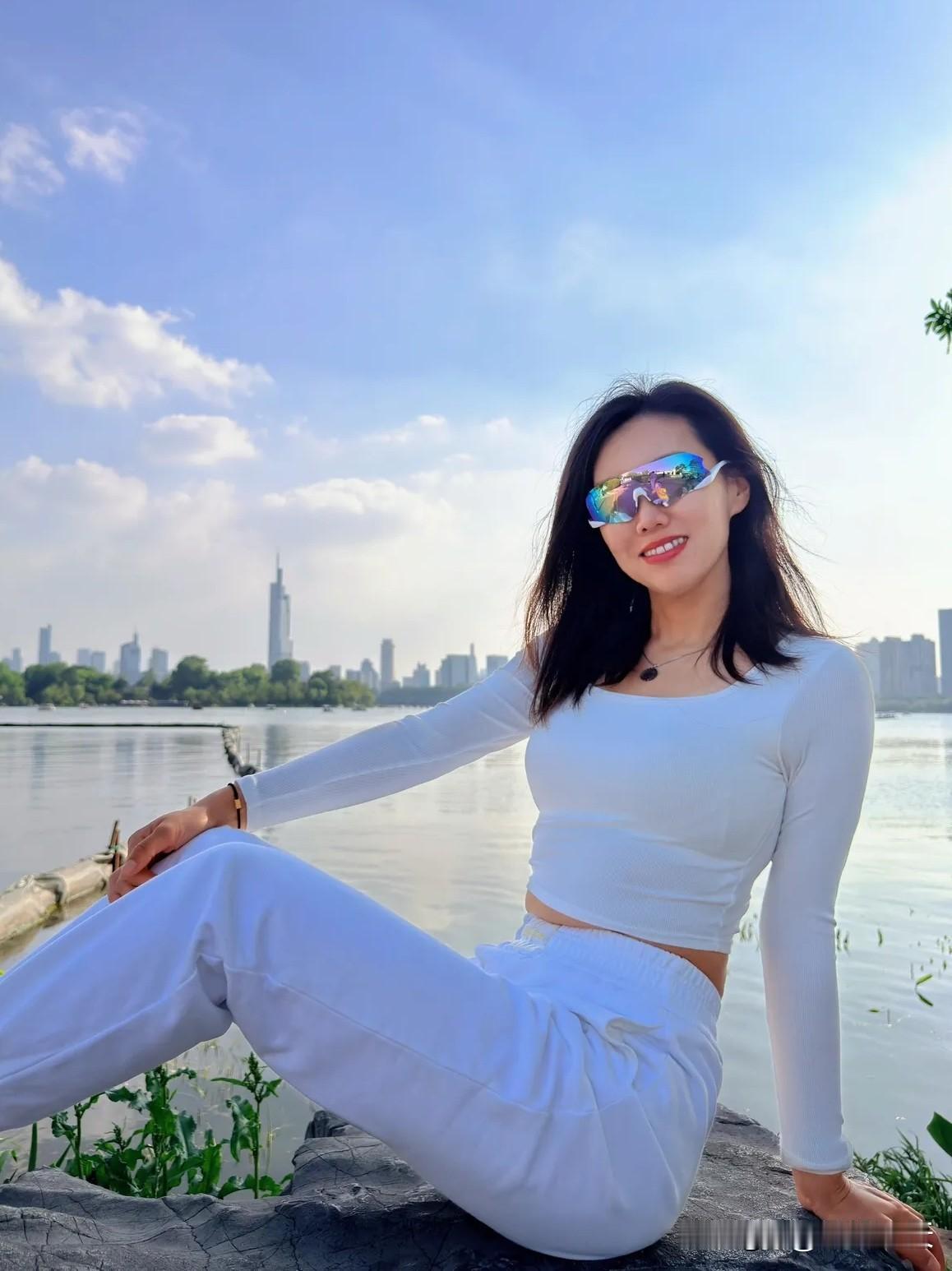 阳光洒在波光粼粼的湖畔，一位白衣少女站在那里，嘴角上扬，露出甜美的微笑，正对着手