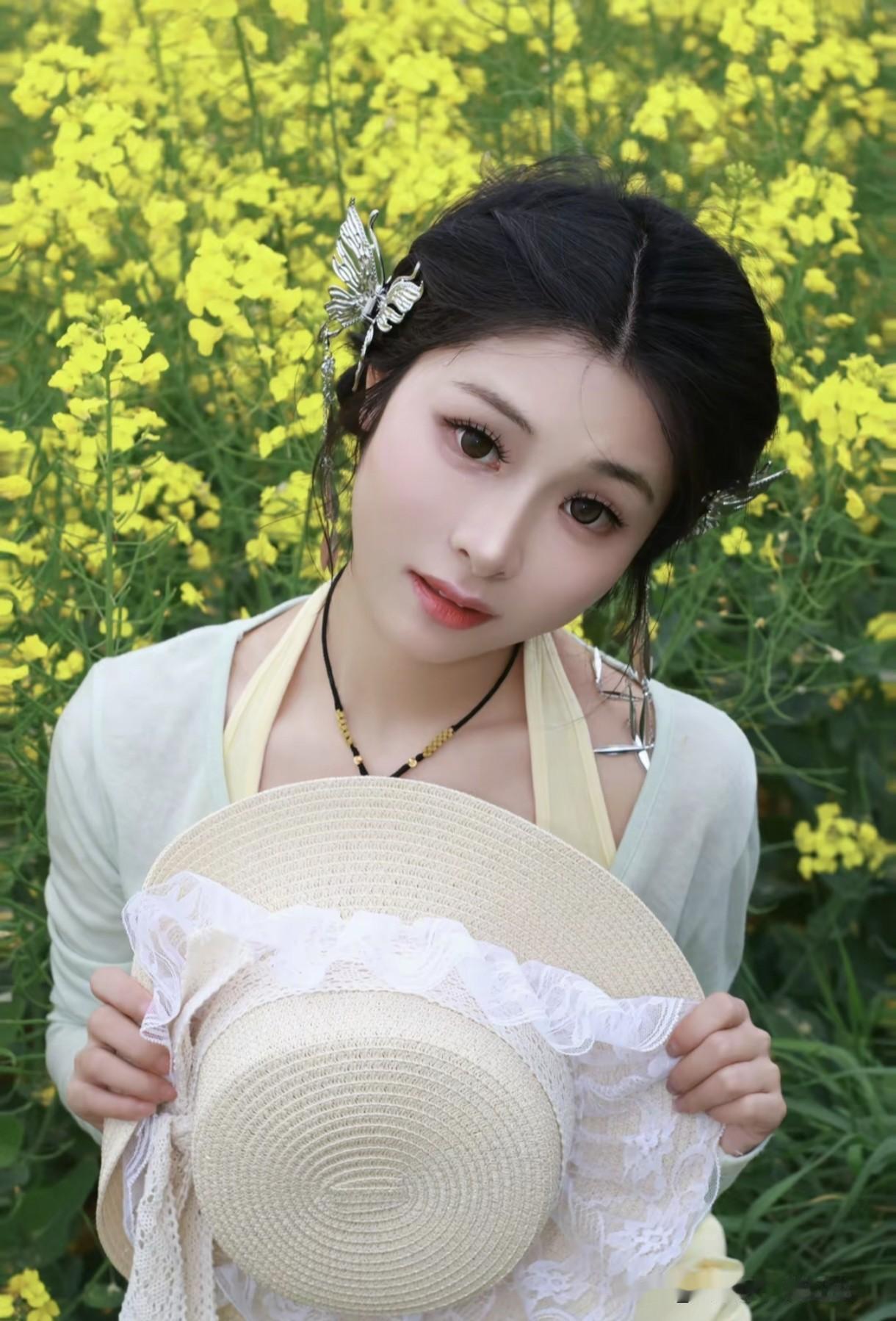 一个带帽子美女田园油菜花姑娘花帽小女孩女孩在油菜花田里拿着帽子。