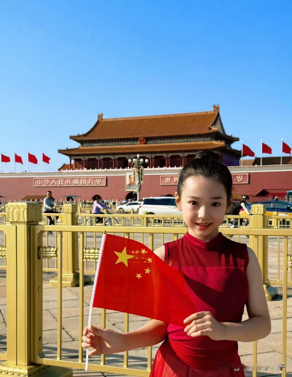 小酒窝（董璇女儿）身穿红裙，扎着丸子头，手里拿着五星红旗，笑容灿烂，迎风挺立，在