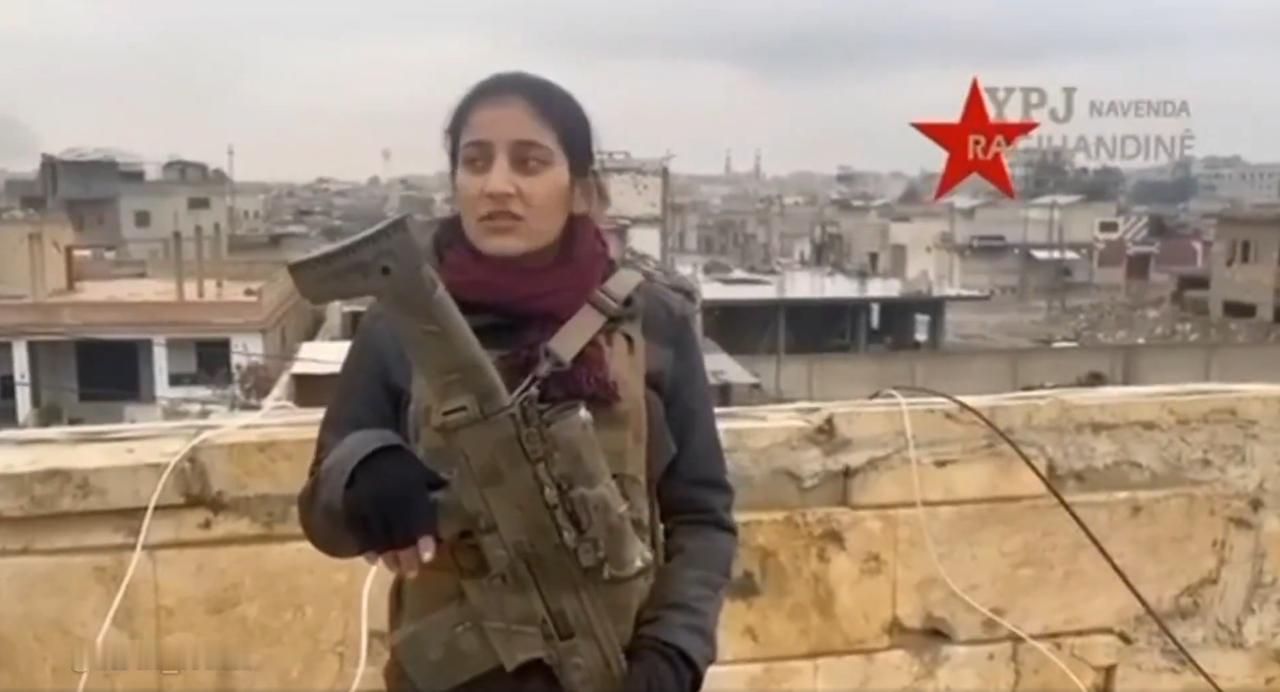 一名YPJ女战士站在拉卡的一处屋顶上，手持一支CZBREN2BR突击步枪，