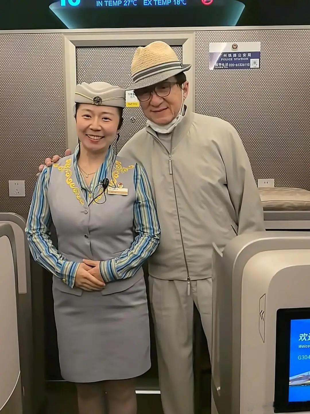 72岁成龙坐高铁出行被偶遇，他坐商务舱，和一名乘务员拍摄了合照。他的穿衣打扮很有