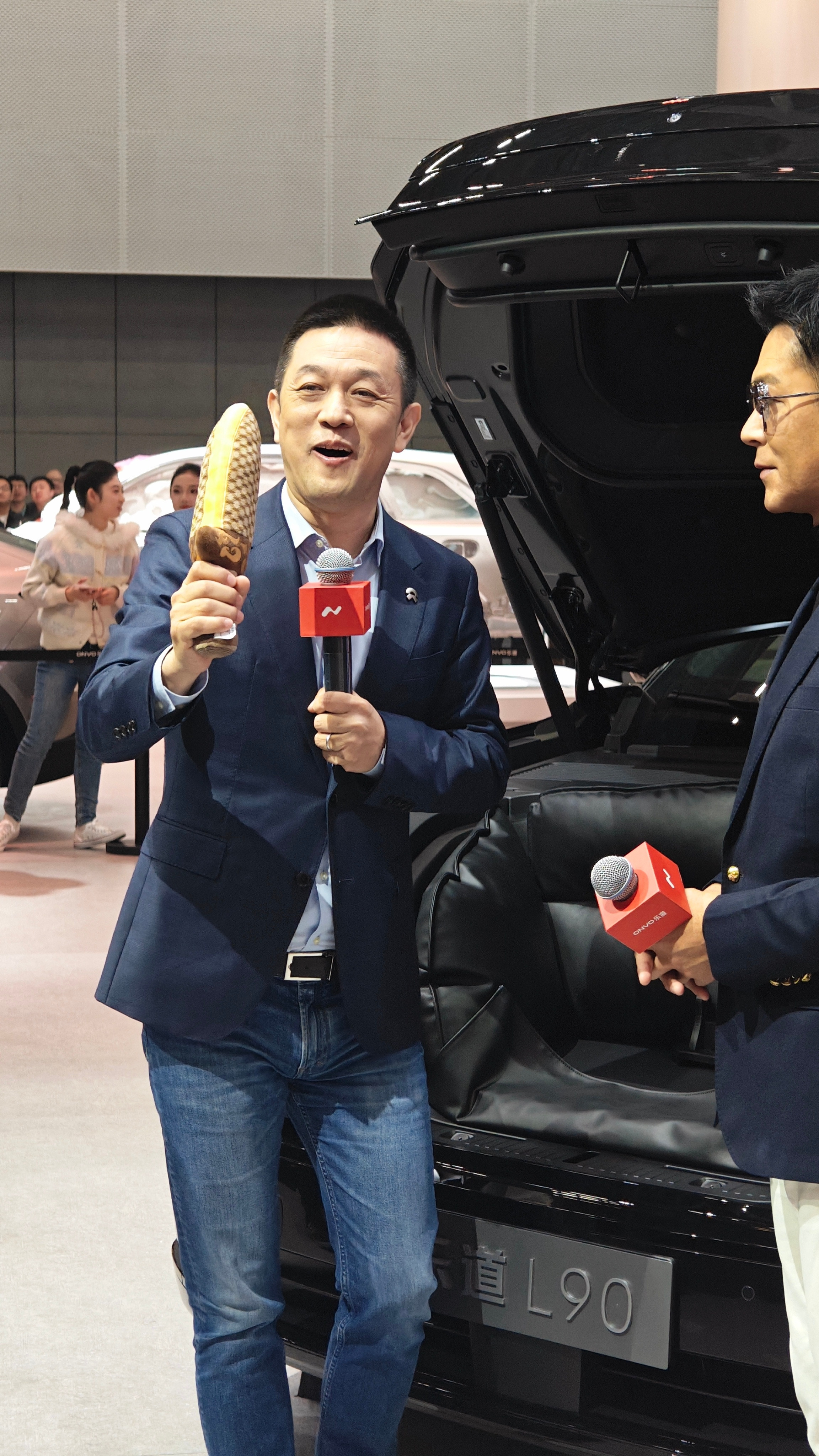 斌哥从乐道L90黑骑士版的前备箱，掏出了一把宝剑（布偶），送给了古天乐，祝他的寻