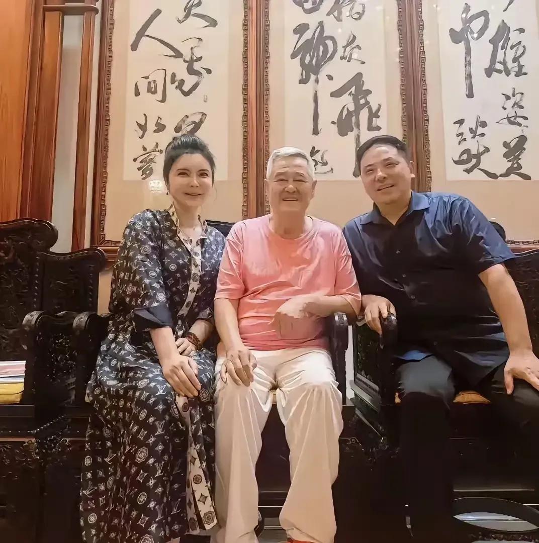 赵老师这位妥妥的老艺术家，穿着粉色的上衣，白色的裤子，坐在中间的位置，虽然头发花