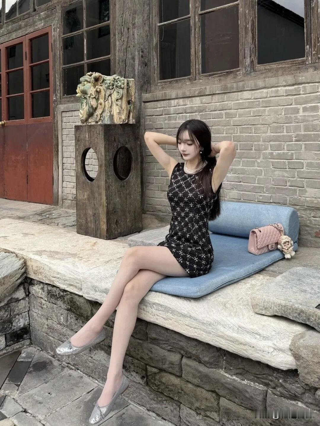 复古砖墙前，黑裙少女优雅坐，静享时光。