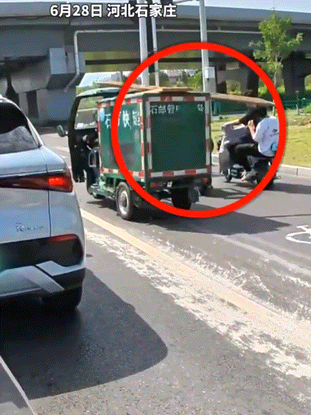 河北石家庄，一小伙骑着电动车在路口等待红绿灯，期间一辆拉着木材的三轮车从小伙旁边