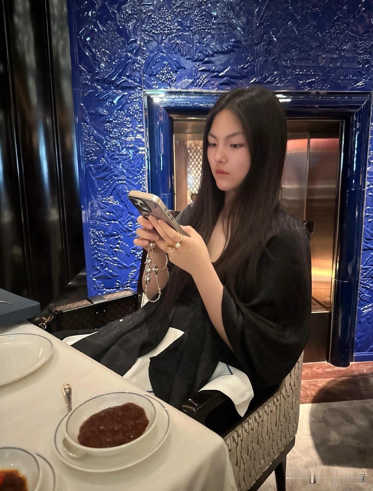 王诗龄假期休息做美甲，穿搭略显成熟～王诗龄身穿宽松黑色长袍连衣裙，手拎棕色花纹小