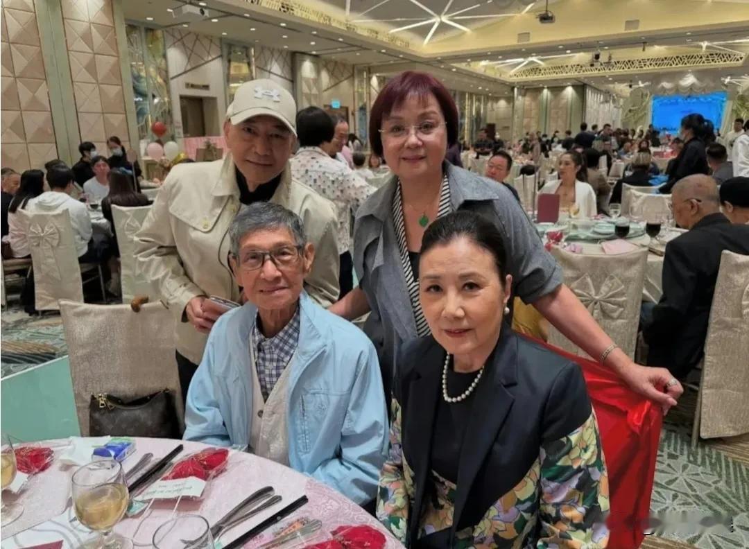汪明荃罗家英一起出席朋友的宴会，汪明荃戴着珍珠项链，穿着花色西装，头发高高盘起，