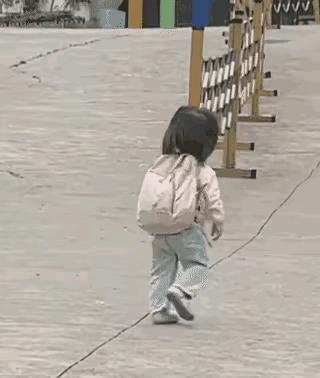 妈妈送幼小的女儿去幼儿园上学，女儿独自向学校走去。大大的背包，小小的身体，蹒跚的