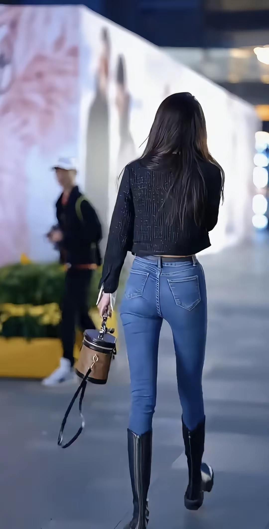 都市女孩的时尚穿搭，蓝色牛仔裤搭配黑色皮靴，手提小包，自信走在街头。