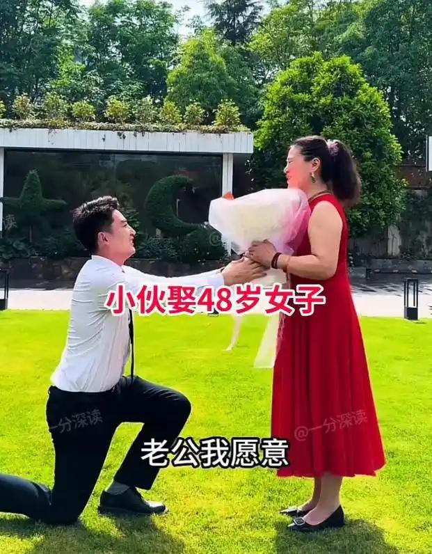 阳光下的草坪上，年轻小伙单膝跪地，手捧鲜花向48岁的她求婚，一句“老公我愿意”，
