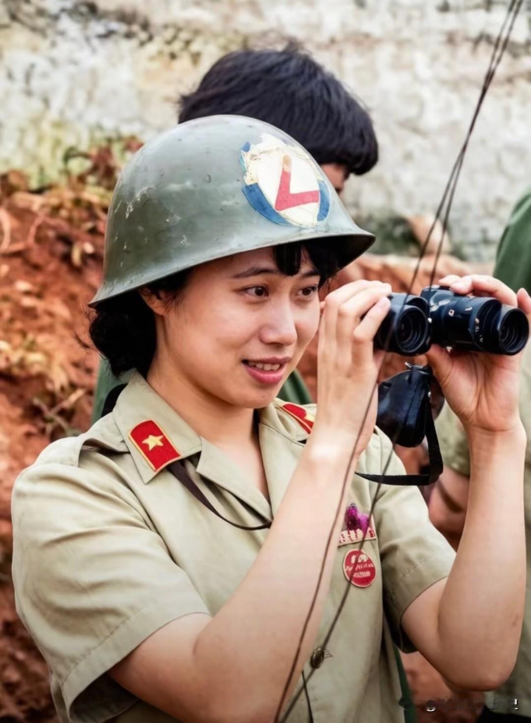 在这张老山前线的留影中，参战女兵刘莹手持望远镜，专注地观察着战场。她身着笔挺军