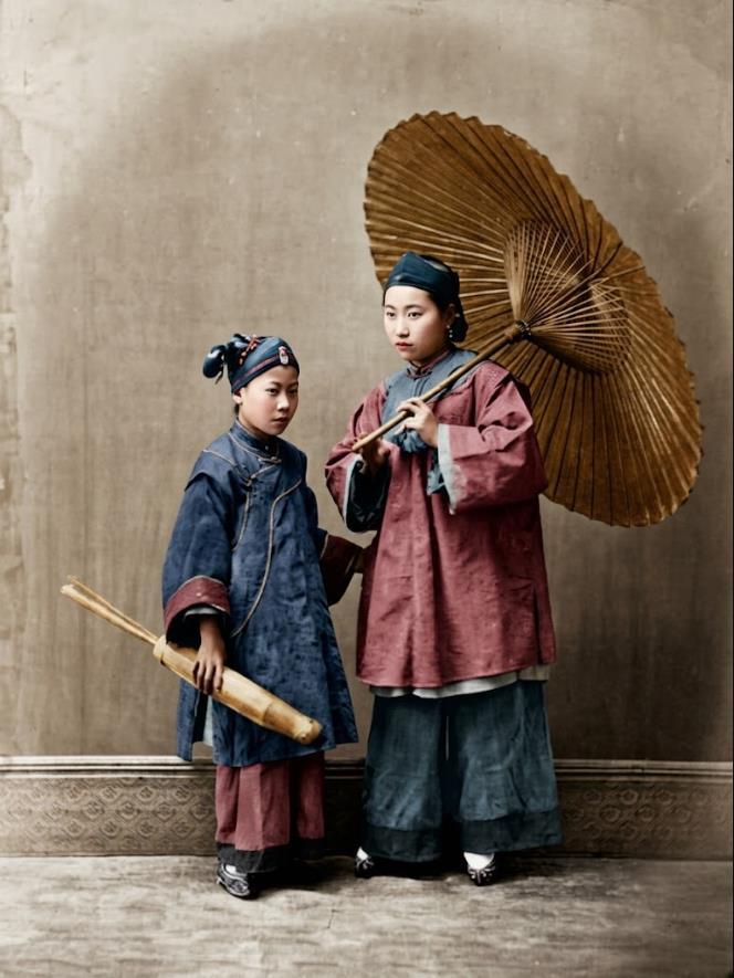 晚清，照相馆内，打着油纸伞的两个女子，右边的女性，身着宽袖大襟袄与宽腿长裤，肩扛