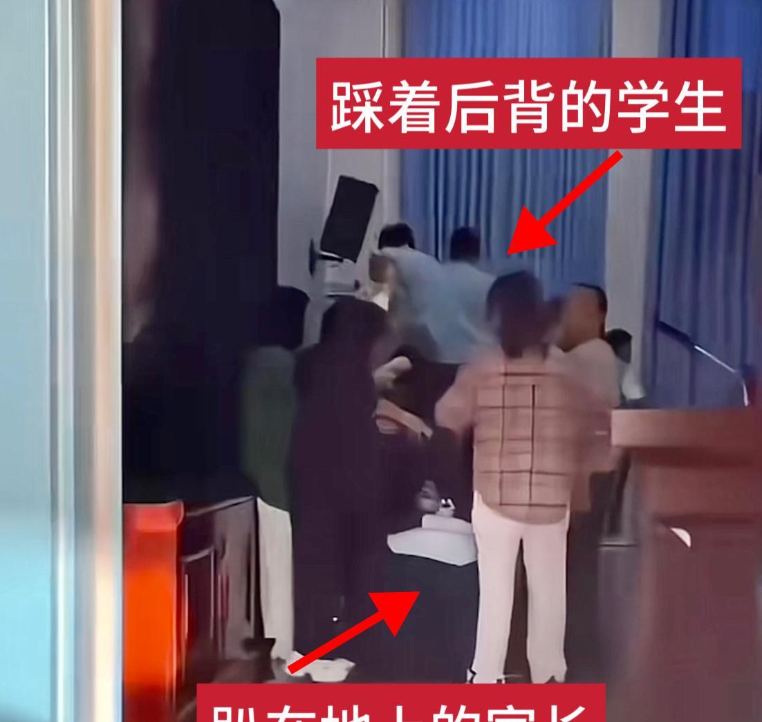 一排家长趴在地上、一队学生踩在家长的后背从一侧走到另一侧、现场还有人用话筒喊着“