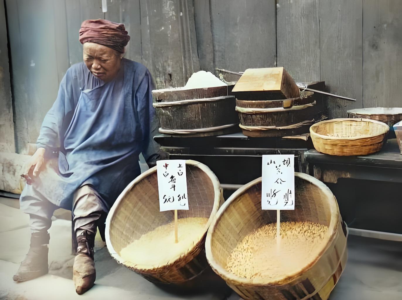 旧中国灾区街头，土坯墙下，一位头戴破旧头巾、身着补丁摞补丁粗布衫的女摊贩，身形佝