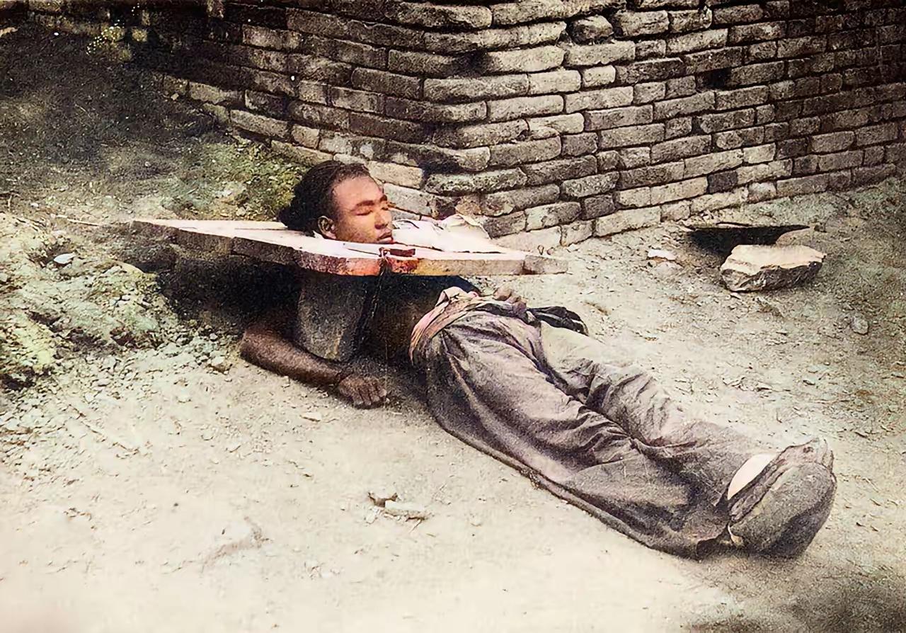 清朝末年，一名戴枷示众的男子，躺在地上睡着了。可能是枷板太沉重，男子在下面支起