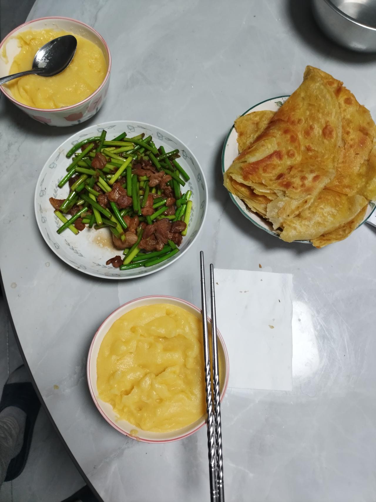 老两口的晚餐很简单。一盘儿蒜毫炒肉。玉米面儿糊糊粥。烙饼可以说是我老