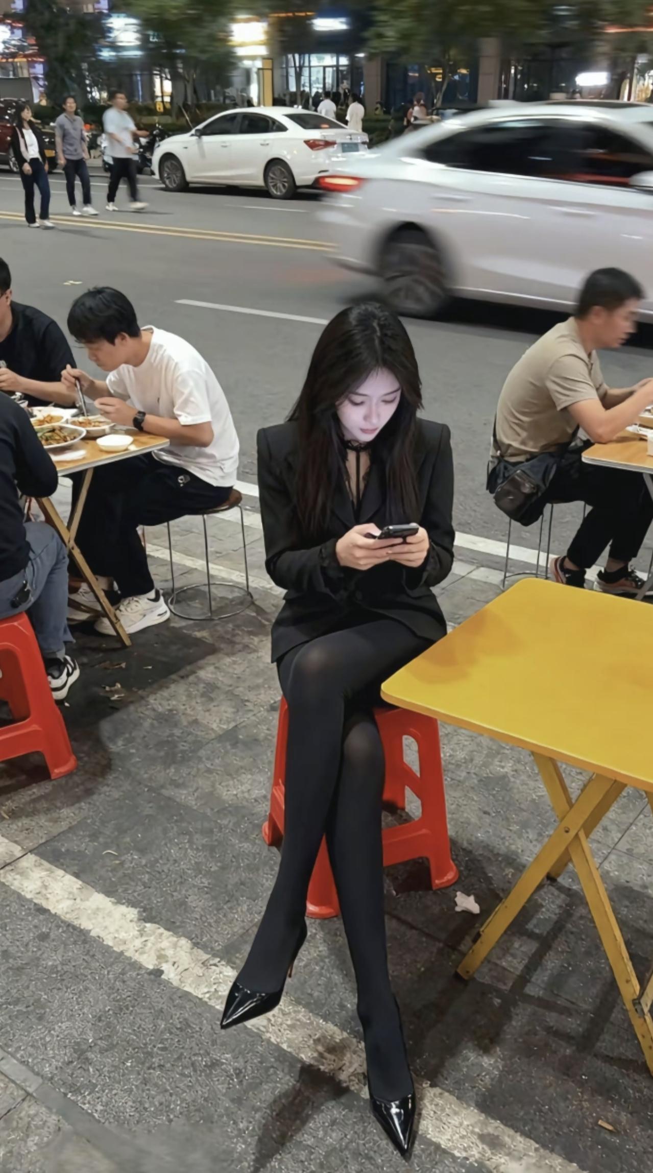 晚风吹过街边的烟火气，黑西装裹着松弛的夜晚。高跟鞋踩在市井的地砖上，手机屏亮着独