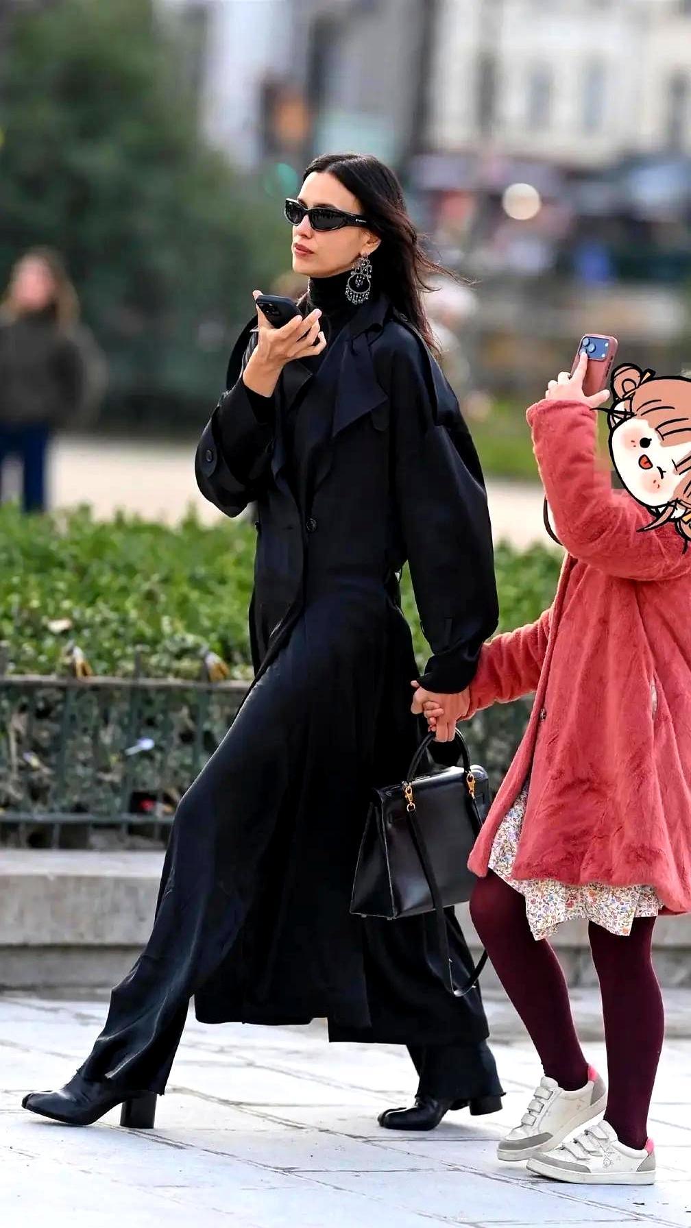 巴黎街头，伊莲娜一身黑，高领毛衣配缎面大衣，阔腿裤踩高跟短靴，墨镜一戴气场两米八