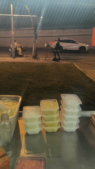 一名男子晚上在街头摆摊卖炒粉炒面。正好他的对面有一个年轻女孩在路边直播跳舞💃
