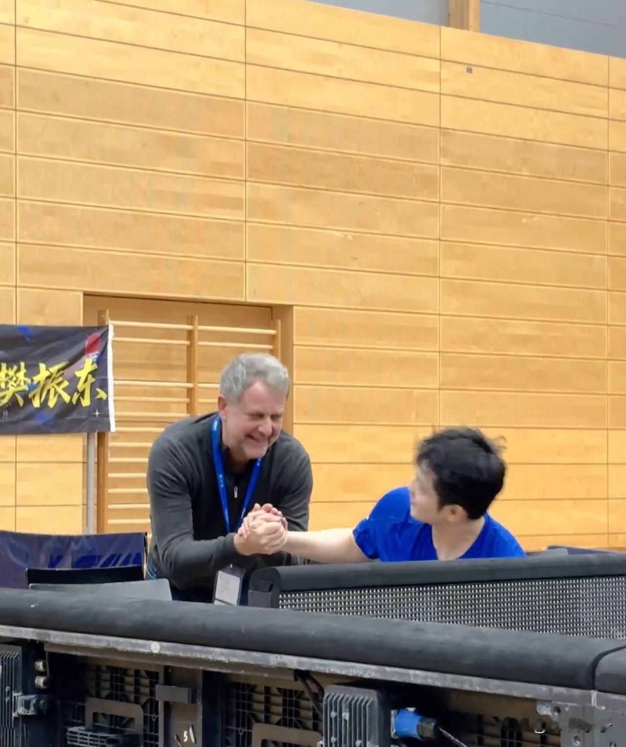 在萨尔布吕肯的热身训练场，两个老人特意过来和樊振东打招呼，原本站着的樊振东非常有