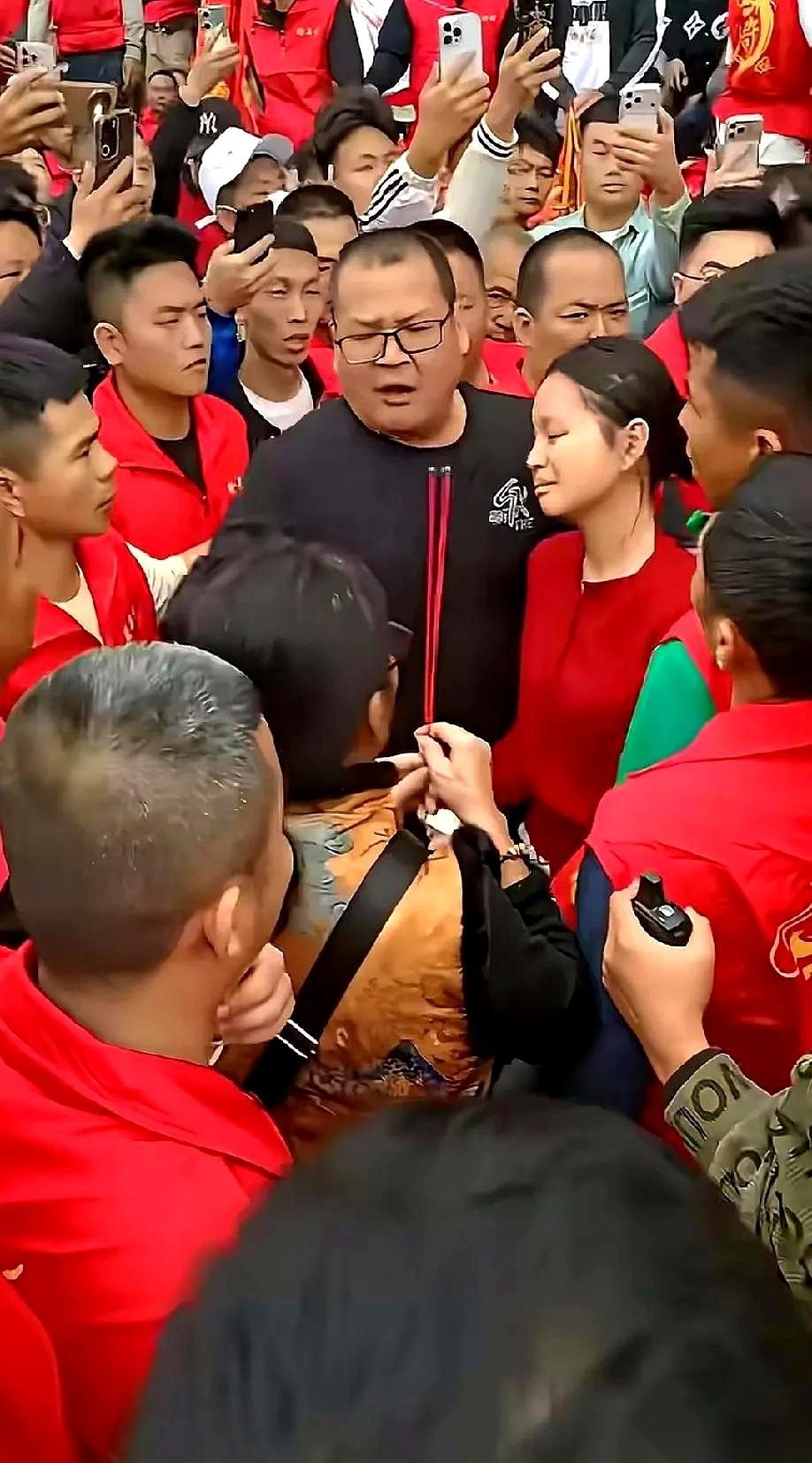 一群穿着“许”字红马甲的男人，死死围住一个小女孩。她爸爸往前挤，想把女儿拉出来