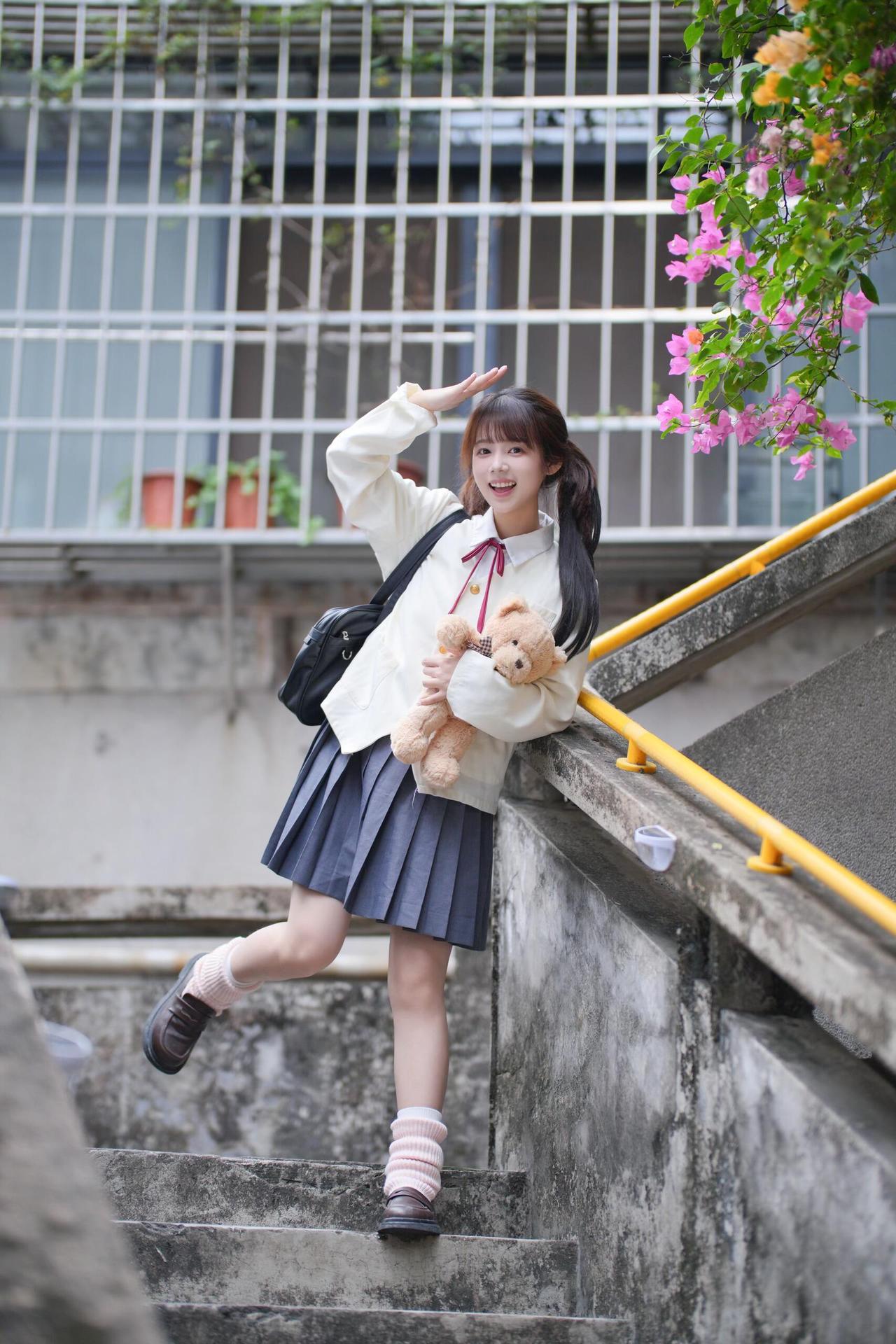 青春洋溢的校园少女，背着书包，手捧小熊，微笑着走上楼梯。