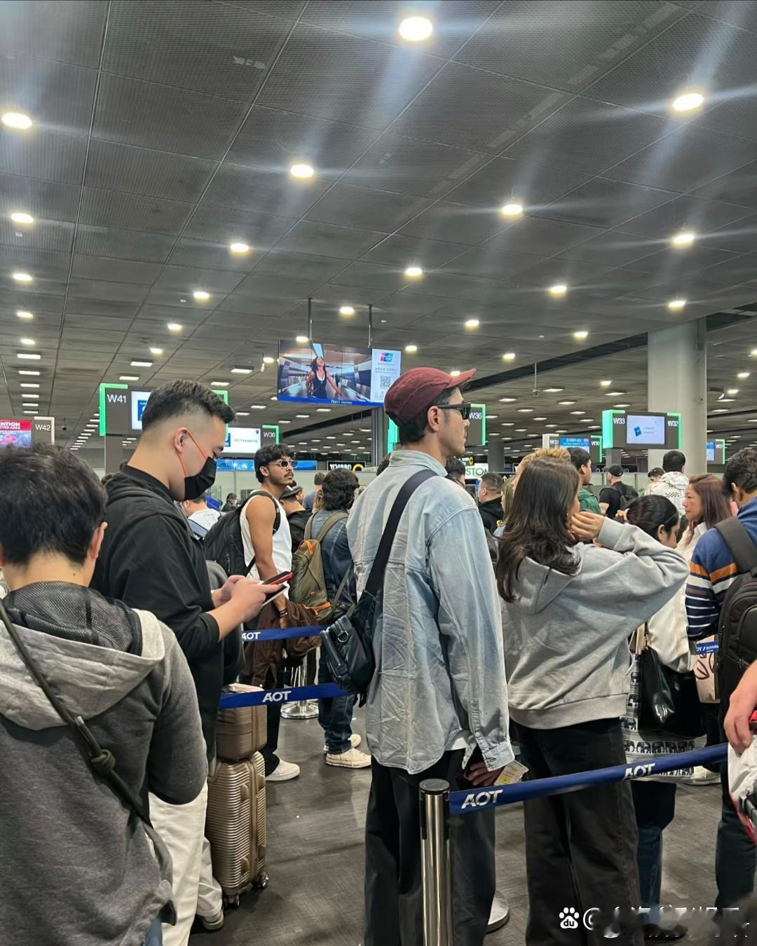 在泰国机场竟然遇到了阮经天，他戴着红色帽子墨镜，穿着牛仔衬衫，背小黑包，站在人群