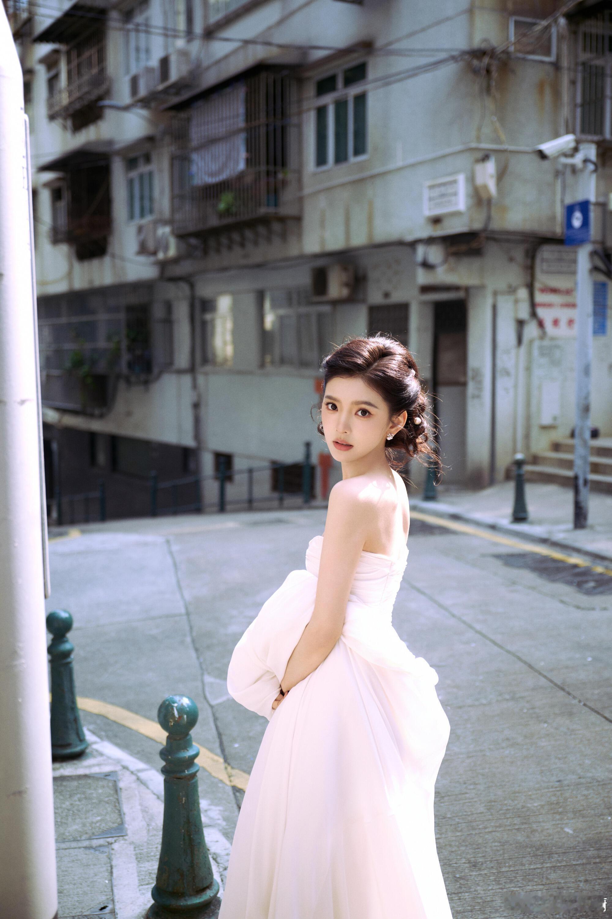 章若楠一袭纯白抹胸长裙裹着明媚气质，珍珠配饰衬出精致甜柔，街巷布景里的微风氛围感