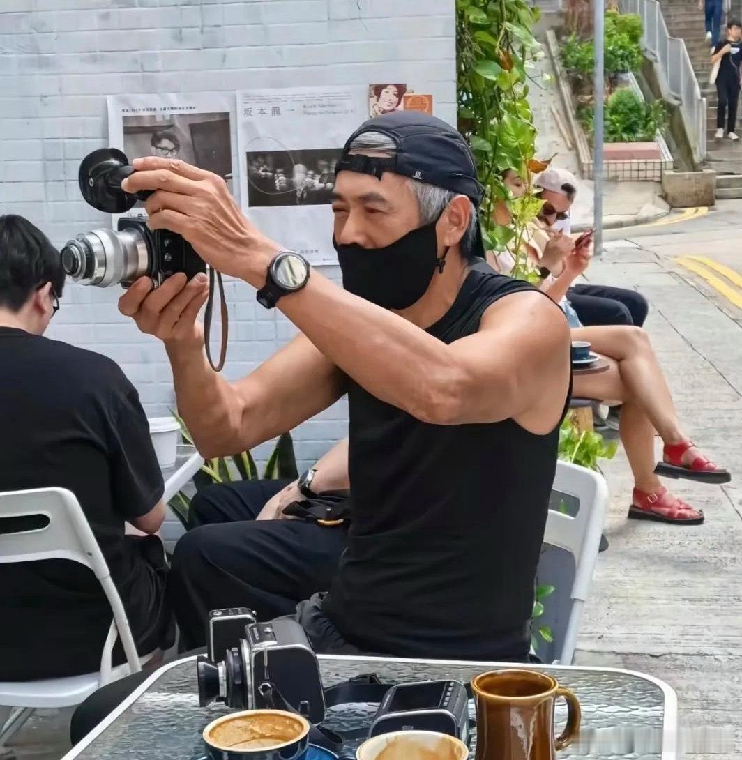 70岁周润发现身香港街头，坐在街边喝咖啡，和朋友们交流摄影技术，看起来好悠闲。他