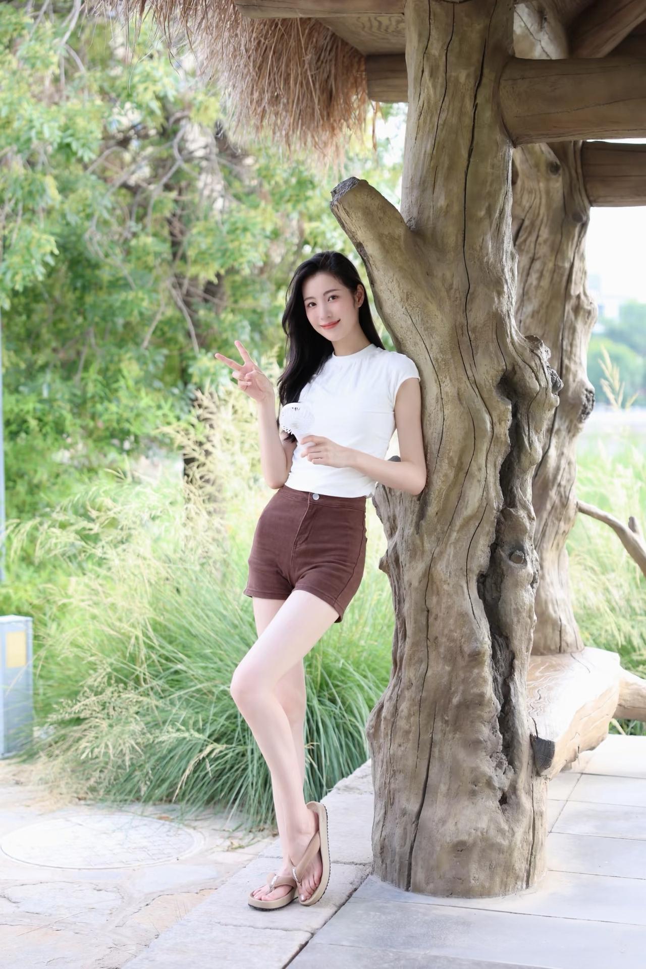 阳光明媚，腿比身子长的她靠在树干上比V字。时尚姐姐图。靓美身姿高挑美女日常写