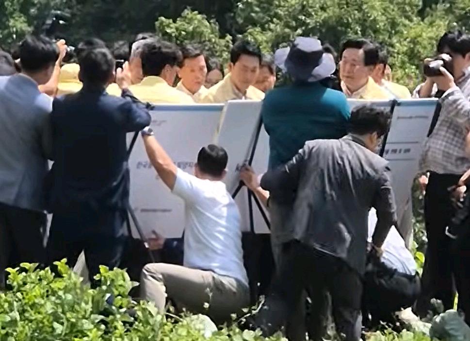 韩国媒体消息，国民力量党张东赫视察旱灾时现场展示面板后面由农村社团官员托举展板遭