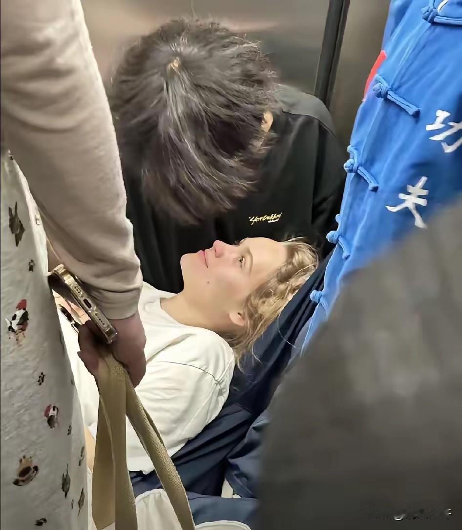 外国女生头晕站不稳，旁边中国男生就让她靠在自己腿上休息，当了临时“人形靠垫”。