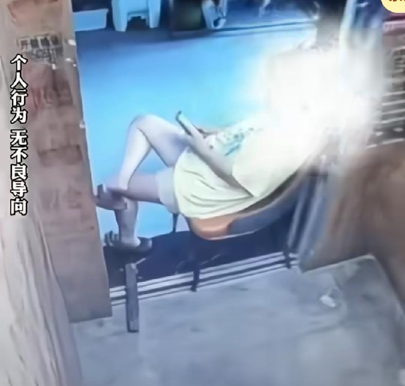 女子为了享受电梯里的空调，坐着玩手机，用椅子卡住电梯门，不让电梯合上，一直停在