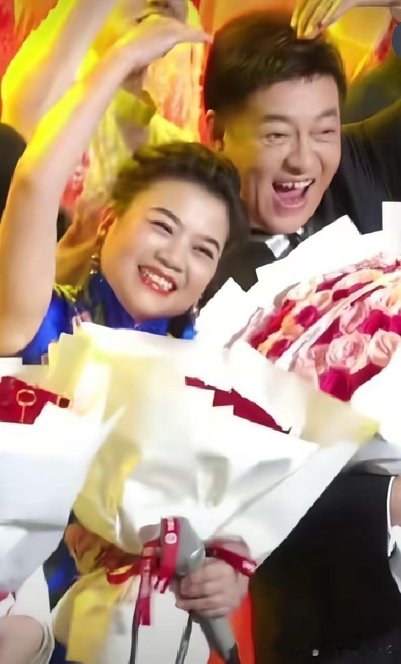 张也、吕继宏两个人手捧着鲜花，比着爱心，在舞台上笑的脸都要开花了。张也长相端