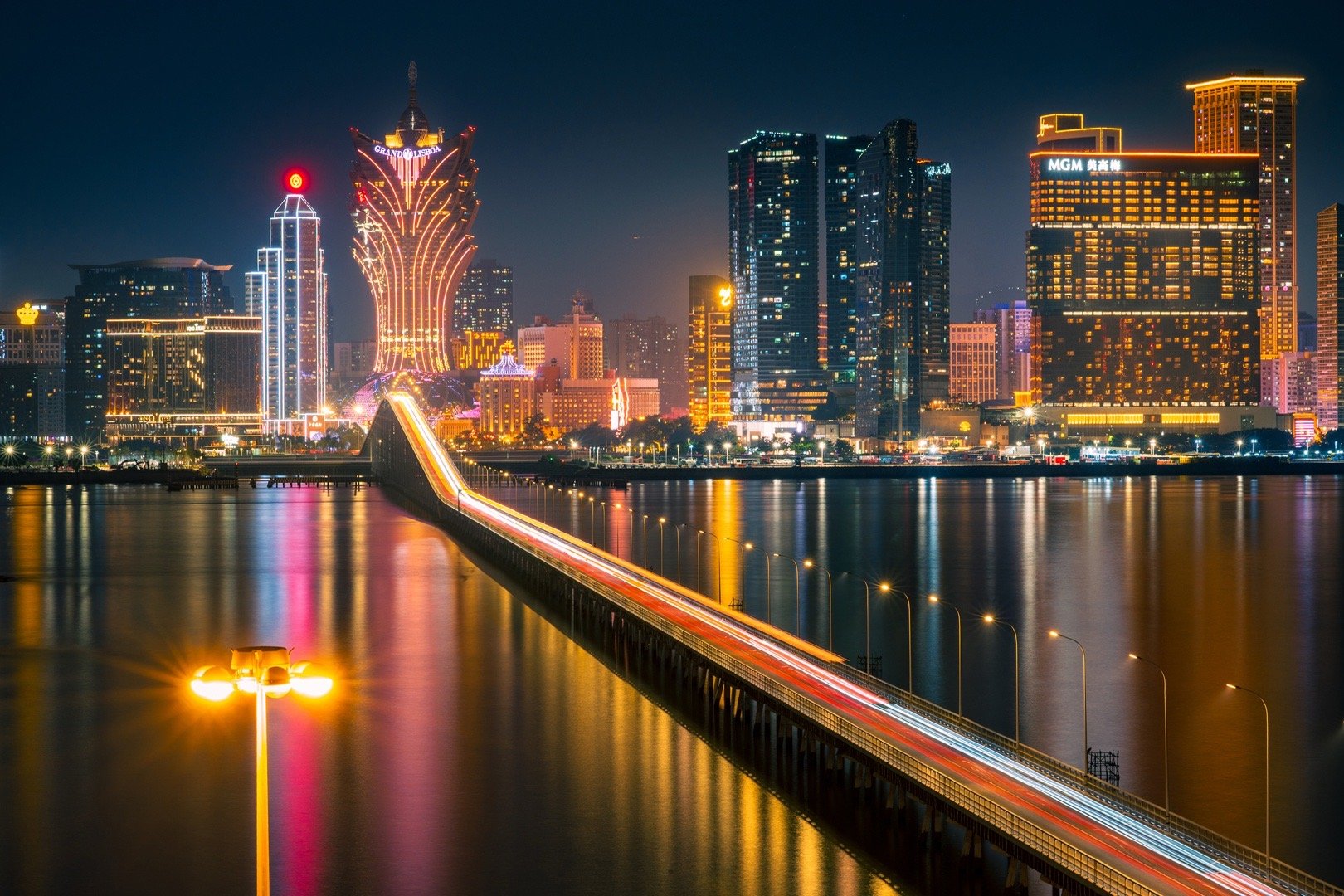 你好，澳门！夜色把濠江揉成一捧碎金，桥上车流拖着光尾划过水面，对岸的霓虹正将城市