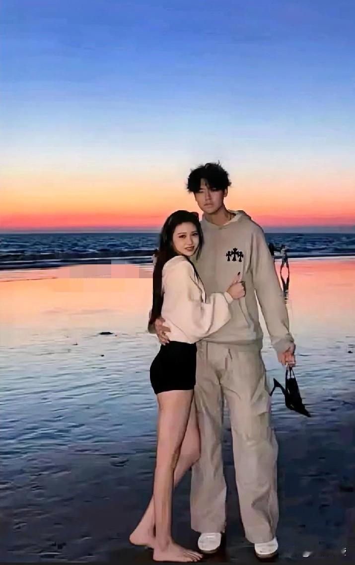 照片中，小苹果依偎在男生身边，男生一手搂着小苹果腰，一手提着小苹果的高跟鞋，两人