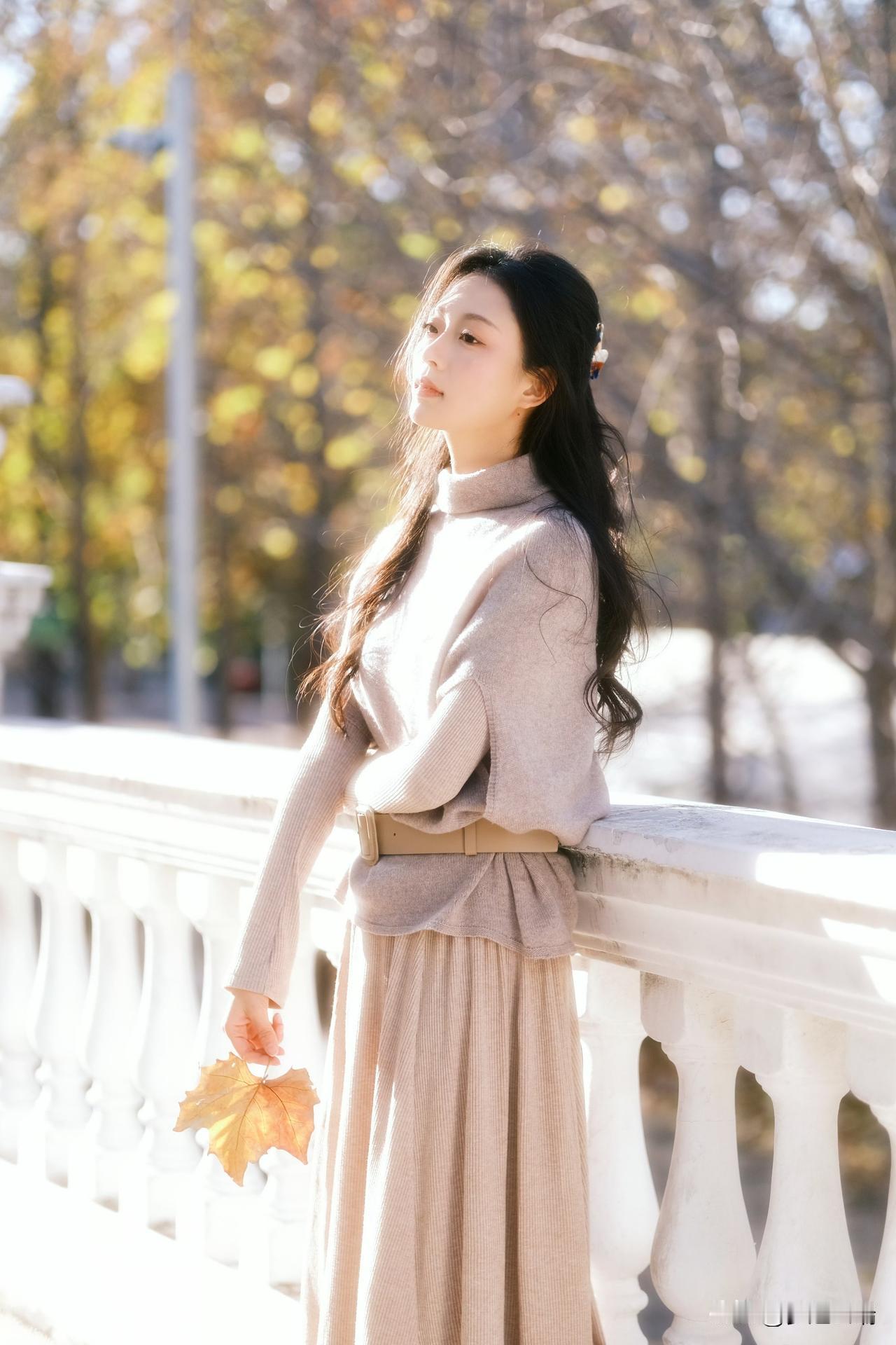 秋日暖阳下，少女轻倚栏杆，手捧落叶，静享时光。