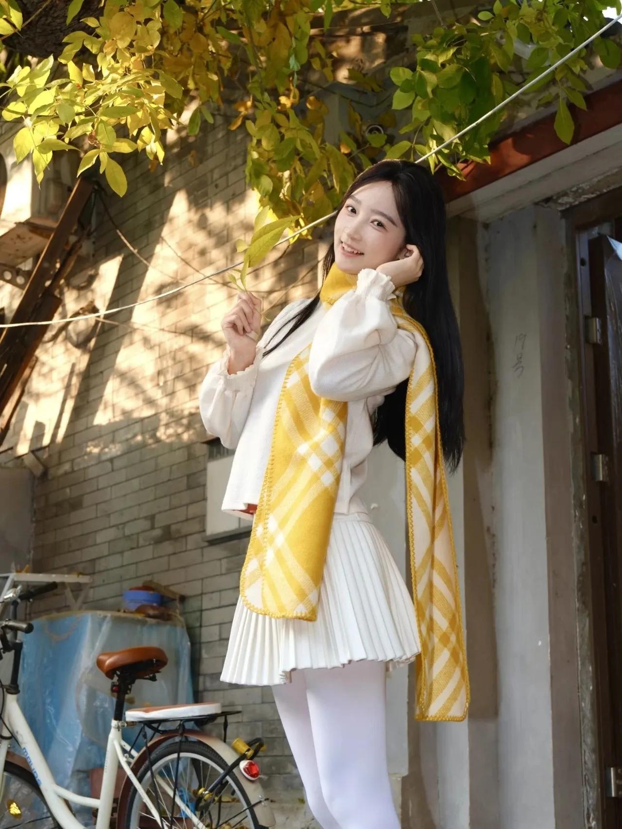 阳光透过树叶洒下来，穿上一身软糯的白色毛衣和百褶裙，再搭配一条亮眼的黄色围巾，你