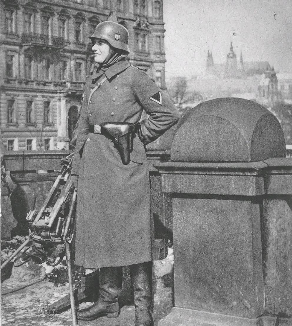 1939年，捷克斯洛伐克，布拉格。一名德军士兵站在街头，头顶钢盔，腰佩手枪，面带