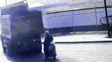 路口闷热时，一个大哥骑着电动车慢悠悠往前晃。对面一辆大货正往后挪，警示灯一闪一