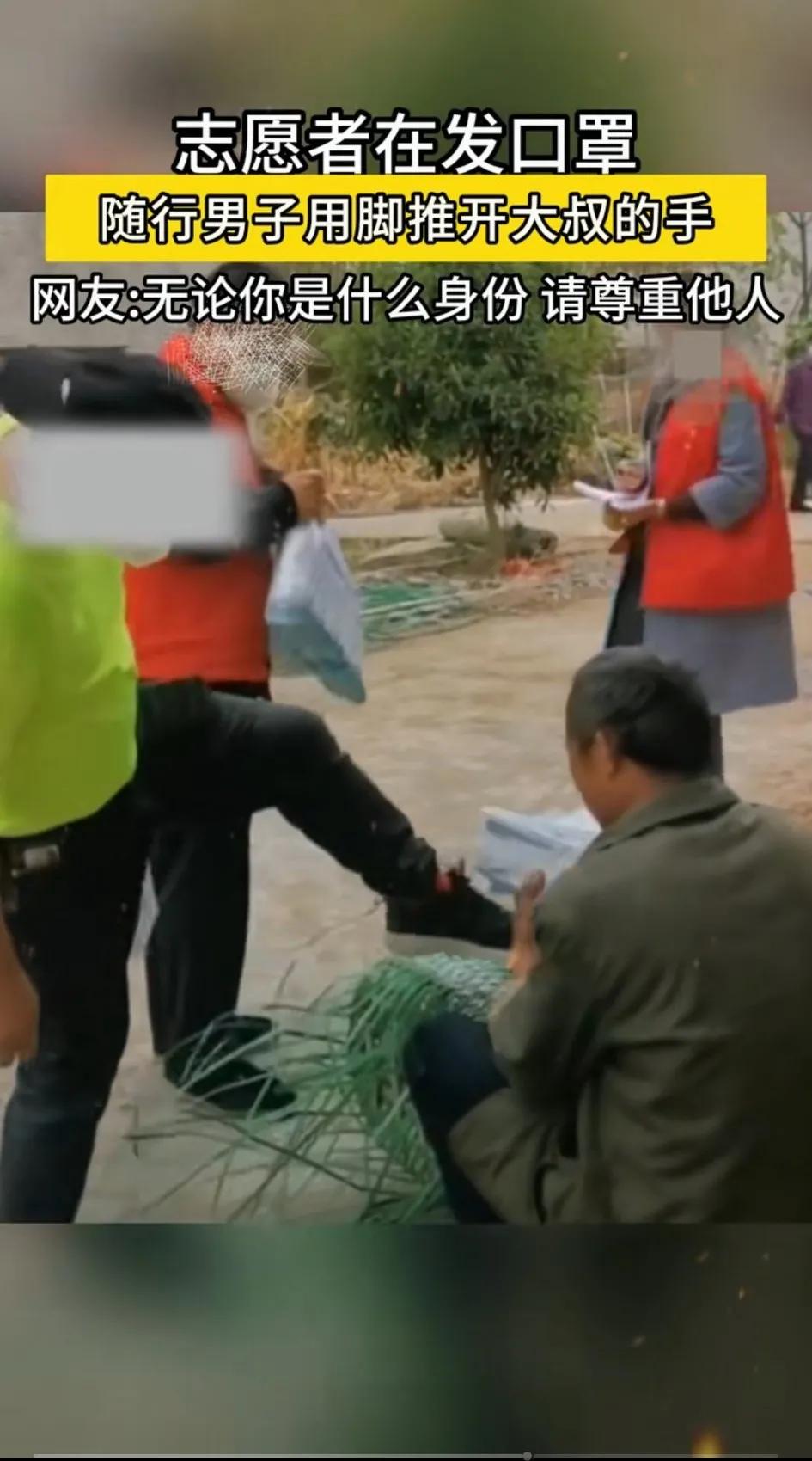 志愿者在发口罩，一大叔在接口罩，也许接口罩的手挡住了他们的视线，随行男子用脚推开