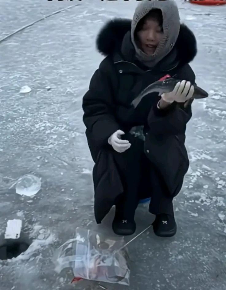 女子开心地展示刚钓上来的鱼，把手机放在了胸前，结果冬天太冷的原因，布料太滑，