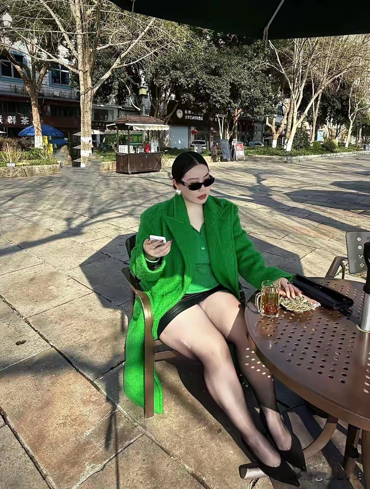 阳光明媚，绿衣女子在户外喝咖啡。