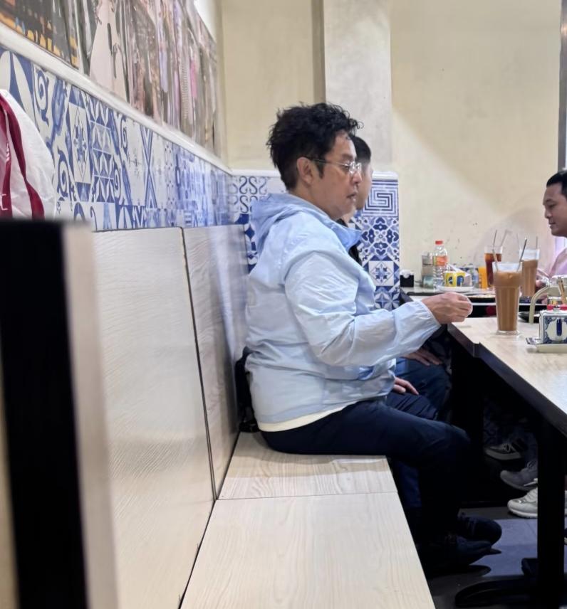 75岁谭咏麟在澳门路环码头一家餐馆吃面，他穿着足球队的衣服，留着一头羊毛卷发，身